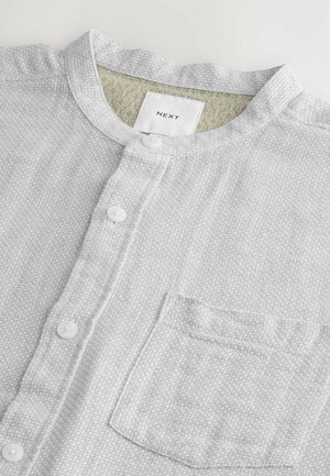 Hellegraues Hemd mit Knopfleiste aus strukturiertem Stoff, Stehkragen, fünf Knöpfen und einer Brusttasche. Die Etiketten zeigen die Marke "NEXT".