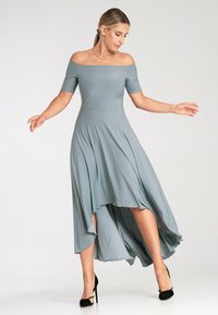 Jasnoszara sukienka bez ramiączek z falującym asymetrycznym dołem, uszyta z miękkiego materiału. Połączona z czarnymi, wysokimi szpilkami.