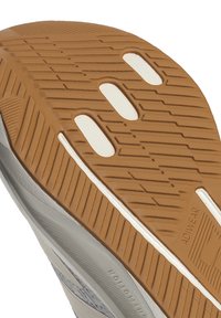 Gros plan sur une semelle de chaussure en caoutchouc brun avec une texture antidérapante, des rainures blanches et le mot "ADIWEAR" embossé.