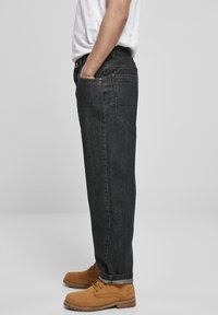 Sorte denimjeans med lige ben, der har sidelommer, baglommer og synlige sømme. Kombineret med lysebrune snørebukser.