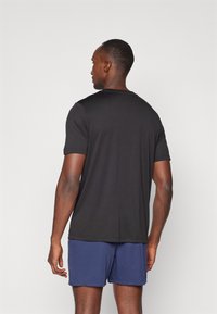 Black short-sleeved t-shirt with a round neckline, made of smooth fabric, paired with navy shorts; visible stitching at the hem.