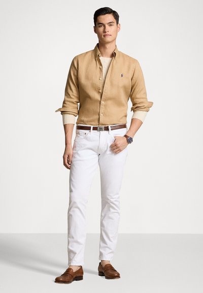Chemise beige à boutons, pantalon blanc, ceinture marron et mocassins marron. Montre au poignet, tissu texturé, coupe ajustée. Design simple, sans motifs.