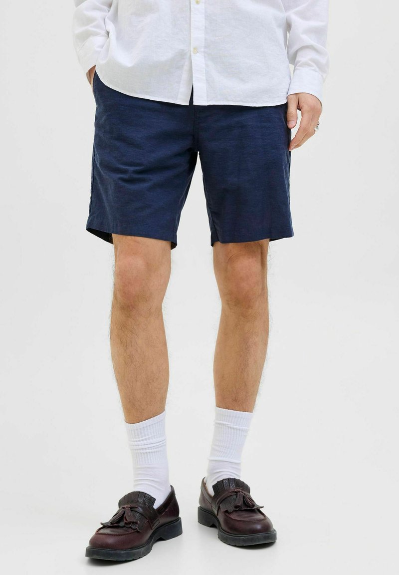 Marineblauwe shorts van lichtgewicht stof met een verstelbare band, gecombineerd met witte sokken en donkerbruine schoenen.