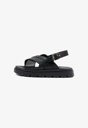 Czarna skórzana sandała z grubą, bieżnikowaną podeszwą, krzyżującymi się paskami oraz regulowaną sprzączką na pasku wokół kostki.