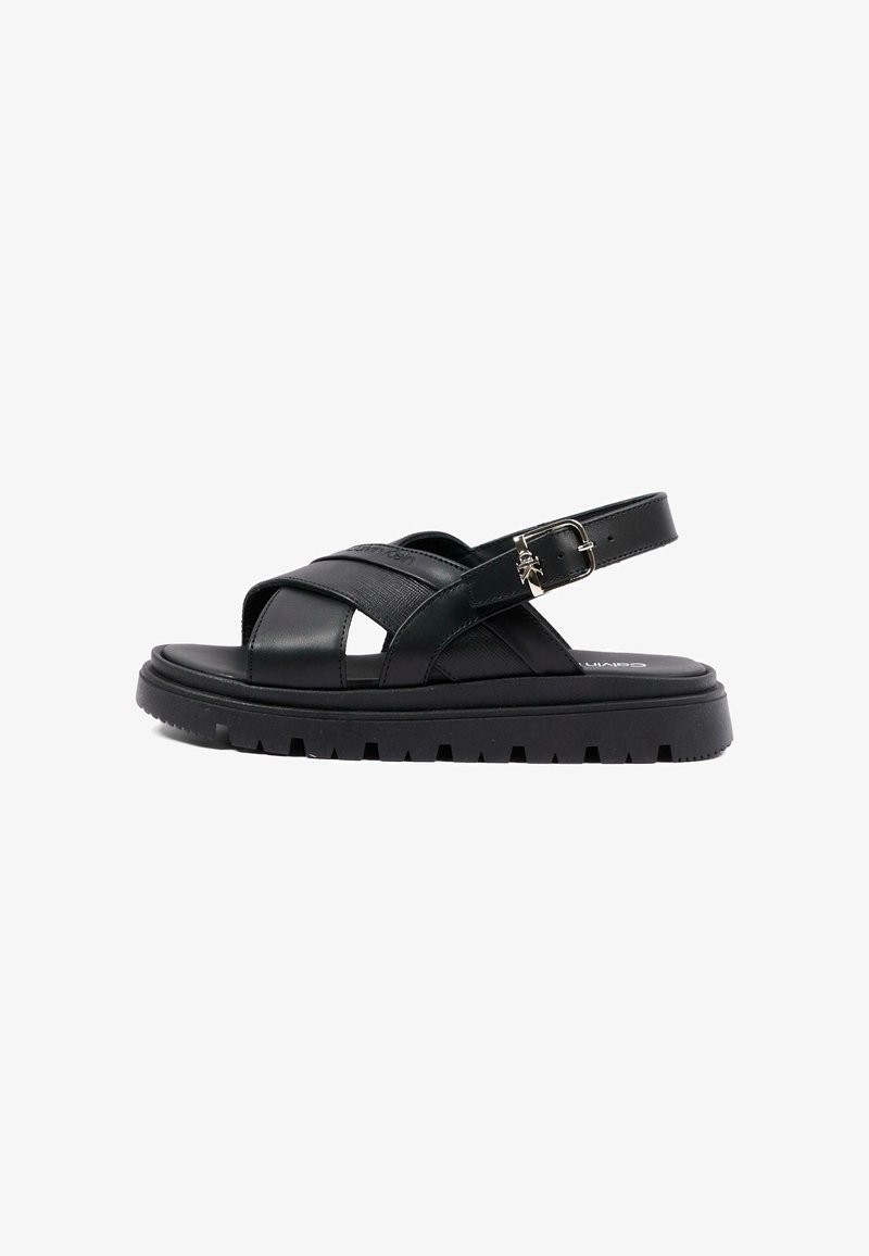 Sandalo nero in pelle con suola spessa e carrarmato, cinturini incrociati e fibbia regolabile sulla caviglia.