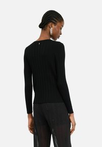 Maglione nero a costine con maniche lunghe e un sottile dettaglio sul retro, abbinato a pantaloni neri trasparenti decorati con accenti lucidi verticali.