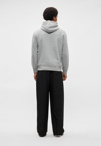 Felpa grigia con cappuccio e polsini a costine, abbinata a pantaloni neri a gamba larga. Texture liscia, palette di colori neutri, design minimal.