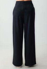 Zwarte wijde broek met een gladde textuur, voorzien van een hoge tailleband en zijzakken, met een losse snit die tot de enkels valt.
