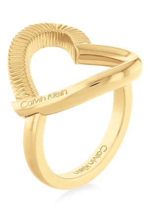Goldfarbener Ring mit strukturiertem Herzdesign. Verfügt über glatte und gerippte Kanten, mit eingraviertem Markennamen "Calvin Klein" auf dem Ringband.