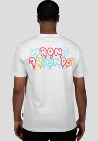 Camiseta de algodón blanca con el texto colorido "WRONG FRIENDS" goteando en rosa, azul, amarillo y naranja en la parte posterior. Mangas cortas.