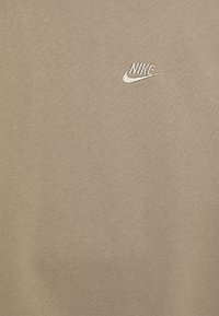 Felpa Nike khaki con tessuto testurizzato, caratterizzata da un piccolo logo ricamato bianco sul petto. Design semplice, senza ulteriori motivi o dettagli.