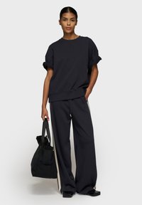 Marineblå oversized sweatshirt med rulleærmer, parret med matchende bredbenede bukser med sideliefer. Bærer en sort totebag.