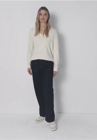 Vaalea beige v-kaula-aukkoinen neulepaita, mustat suorat farkut, valkoiset lenkkarit. Neulepaidassa on pitkät hihat; farkuissa on etutaskut ja pehmeä pinta.