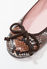 Chaussure plate avec un motif serpent marron, noir et crème, et un nœud en corde marron foncé sur l'avant arrondi, doublure intérieure rose visible.