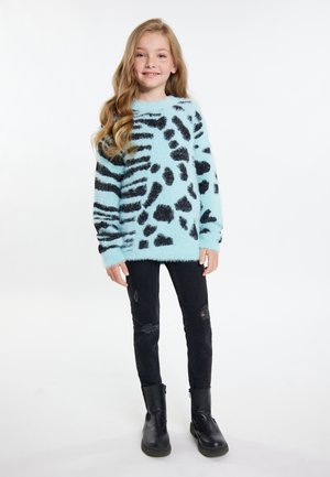 Hellblauer, flauschiger Pullover mit schwarzem Tiermuster, kombiniert mit distressed schwarzen Jeans und schwarzen Stiefeletten. Weiche Textur und oversize Passform.