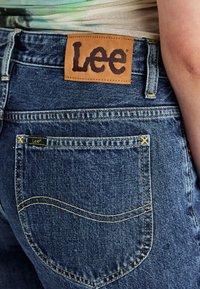 Jeans in denim blu con etichetta in pelle con il marchio "Lee" sulla cintura posteriore. Dettagli in cucitura gialla sui taschini.