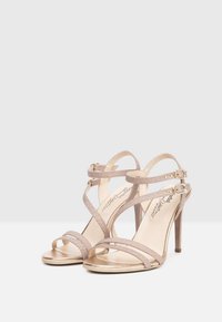 Stiletto sandaler med remme i metallisk roseguld. Funktioner tynde remme med spænde detaljer og et åbent tådesign. Glat, skinnende overflade.