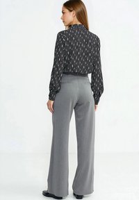 Bluzka w czarno-biały wzór z wysokim kołnierzem i długimi rękawami, zestawiona z szarymi, szerokimi spodniami z wysokim stanem. Gładka faktura.