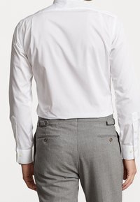 Valkoinen pitkähihainen paita suoralaitaisella kauluksella, yhdistettynä harmaisiin housuihin, joissa on napillinen takatasku ja vyölenkit. Sileä pinta.