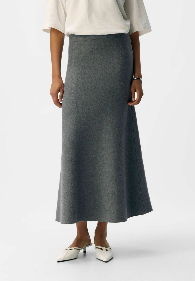 Gray, wool-blend midi skirt with a straight silhouette, featuring a smooth texture and a high waistband, paired with white, pointed-toe mules.