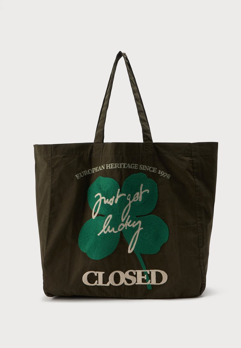 Sac cabas vert foncé avec longues anses, avec un grand trèfle à quatre feuilles vert et le texte "Just get lucky," "European Heritage Since 1978," et "CLOSED."