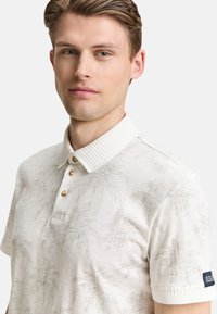Camisa polo blanca con un cuello de canalé, tapeta de tres botones y un sutil patrón de palmeras. Confeccionada con una tela transpirable y de textura suave.