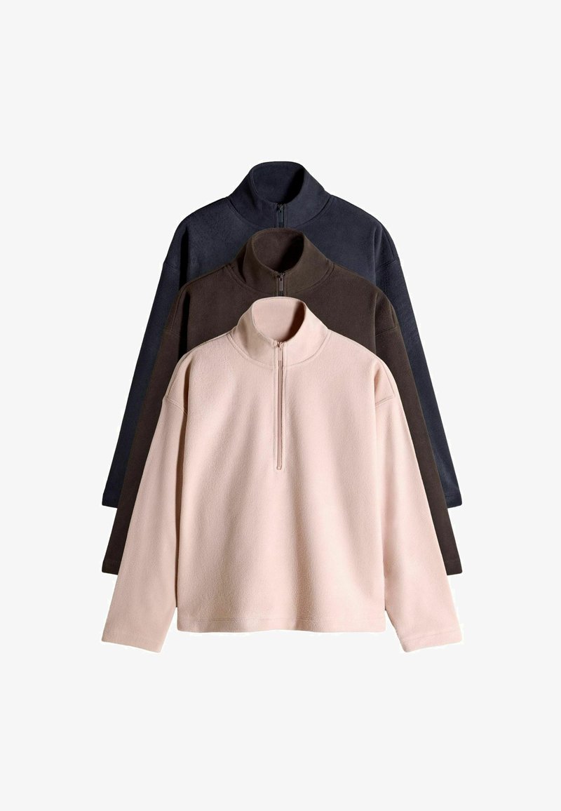 Three fleece pullovers in light pink, dark brown, and navy. Each features a high collar and front zipper, with a soft, textured material.