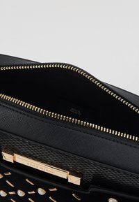 Czarna torba z złotymi elementami i zamkiem błyskawicznym, posiadająca teksturowaną zewnętrzną powierzchnię oraz podszewkę wewnętrzną. Zawiera metkę marki wewnątrz.