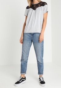 Top gris de manga corta con detalle de encaje negro en el escote, combinado con jeans de denim azul claro enrollados y zapatillas negras.