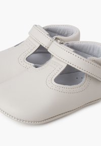 Zapatos de cuero beige claro con punta redondeada, cortes verticales y una correa. Forro interior suave. Costura detallada alrededor de los bordes.