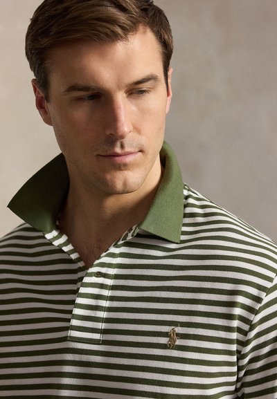 Νεαρός άνδρας κοιτάζει προς τα κάτω, φοράει πράσινο-λευκό ριγέ πόλο με ανεβασμένο γιακά και κεντημένο λογότυπο αλόγου στο στήθος.