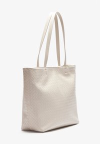 Vævet beige tote taske med to lange håndtag, der har en glat overflade og en struktureret rektangulær form.