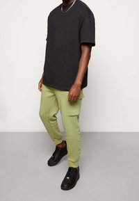 Černé bavlněné tričko s volnějším střihem, v kombinaci se světle zelenými vojenskými kalhotami s bočními kapsami a černými teniskami.