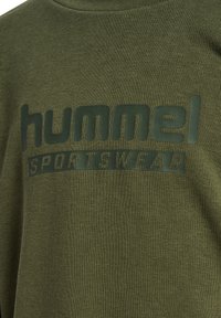 Olivgrüner Sweatshirt aus strukturiertem Stoff. Mit einem auffälligen dunklen "hummel SPORTSWEAR" Logo über der Brust.