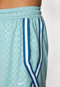 Light blue sports shorts with a textured pattern, featuring dark blue and white side stripes and an elastic waistband. Nike logo visible.