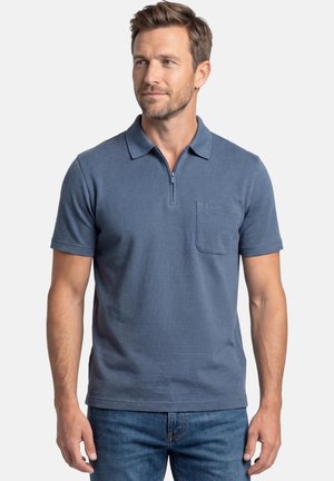 Mand iført en blå kortærmet polo med lynlåslukning ved kraven og brystlomme, kombineret med blå jeans.