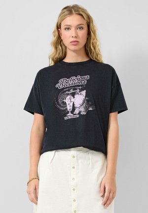 Kobieta w czarnej koszulce z nadrukiem kotka i lodów oraz napisem "Delicious Decisions", w połączeniu z białą, zapinaną na guziki spódnicą.