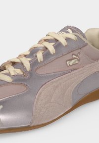 Close-up of a light pink and beige Puma sneaker with cream laces and a gum sole, showing the Puma logo on the side and tongue.