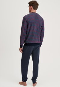 Pull en rayures navy, rouge et turquoise ; texture douce ; associé à un pantalon de survêtement navy uni ; coupe décontractée ; sans matériel visible.