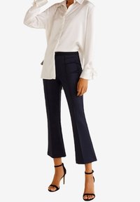 Witte lange mouw button-up shirt met een ontspannen pasvorm, gecombineerd met op maat gemaakte marineblauwe pantalon en zwarte haksandalen. Minimalistisch ontwerp.