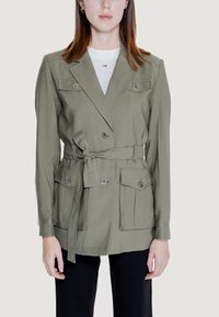 Giacca verde oliva con cintura, design doppiopetto, due tasche sul petto, bottoni argentati e una texture di tessuto liscia.