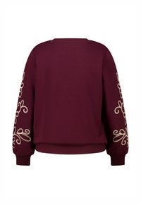 Bordeaux sweatshirt met lange mouwen, met crèmekleurige geborduurde ontwerpen op beide armen en een geribbelde tailleband aan de onderkant.