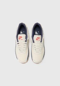 Nike Air Max sportbačiai su kreminiu viršumi, tamsiai mėlynomis detalėmis, baltais raišteliais ir tekstūruota guma, turinčia matomą oro vienetą.