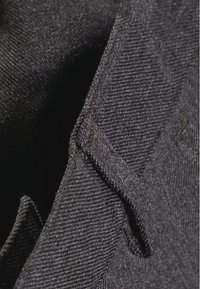 Črna denimska tkanina z teksturiranim tkanjem, ki vsebuje manjši detajl žepne pregrade. Material se zdi robusten in trpežen.