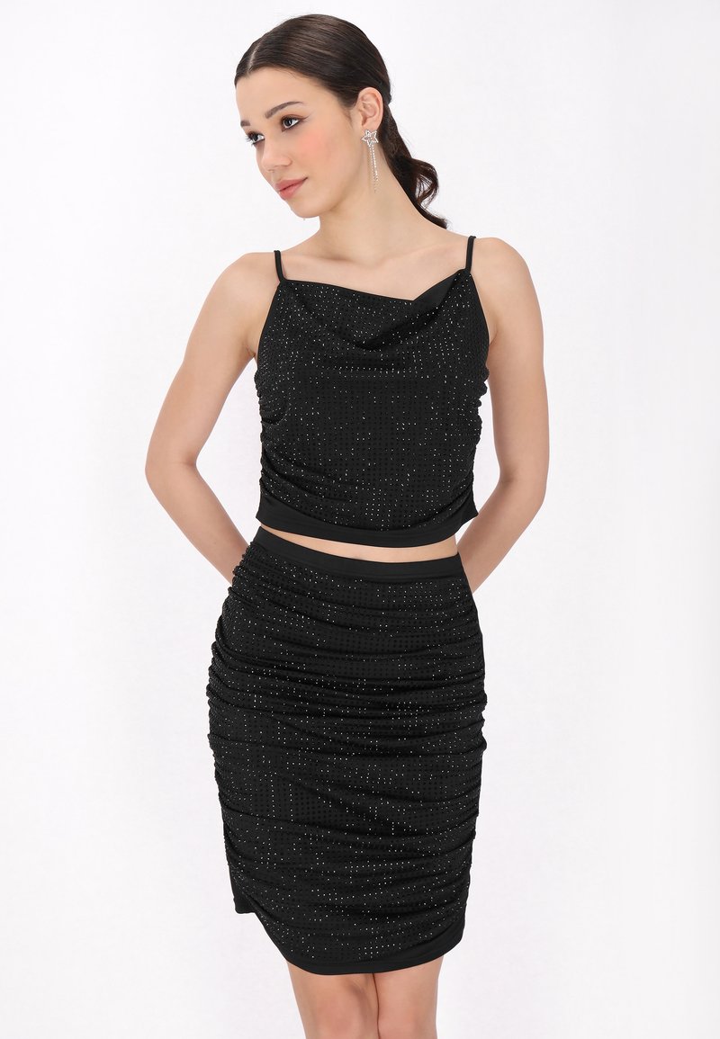 Set in due pezzi nero composto da una gonna arricciata e una top senza maniche drappeggiato decorato con piccoli dettagli in argento. Tessuto morbido e liscio.