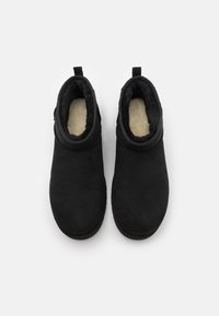 Botines negros con exterior de ante suave, forro interior acolchado y suelas planas. Incluyen un asa para facilitar su uso. Sin cierres visibles.