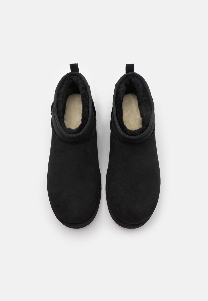 Bottines noires en cuir suédé avec un extérieur doux, une doublure intérieure moelleuse et des semelles plates. Équipées d'une boucle pour un enfilage facile. Sans fermetures visibles.