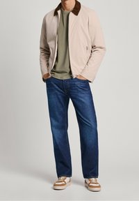 Lyserød bomberjakke med en brun krave, olivengrøn t-shirt, blå jeans og brune og cremefarvede sneakers. Casual outfit med en afslappet pasform.