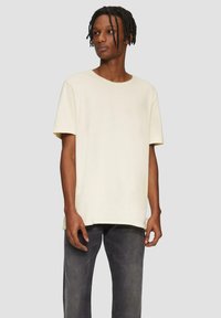 Crème kleurige T-shirt met korte mouwen en een ronde hals, gemaakt van zachte stof, gecombineerd met grijze spijkerbroek. Eenvoudig ontwerp, relaxte pasvorm.