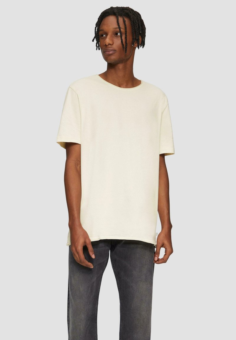 Crème kleurige T-shirt met korte mouwen en een ronde hals, gemaakt van zachte stof, gecombineerd met grijze spijkerbroek. Eenvoudig ontwerp, relaxte pasvorm.